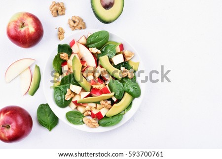 Fruit salad with red apples, avocado, spinach and walnut on light background with copy space, top view. Flat lay.
