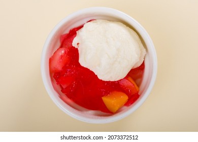 Fruit Salad With Red Or Raspberry Jelly Or Gelatin And Vanilla Ice Cream On A White Bowl On Beige Background Or Cream Background Or Light Yellow Background. Flat Lay. Top View.