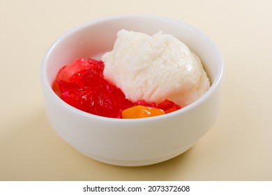 Fruit Salad With Red Or Raspberry Jelly Or Gelatin And Vanilla Ice Cream On A White Bowl On Beige Background Or Cream Background Or Light Yellow Background. Closeup. Side View.