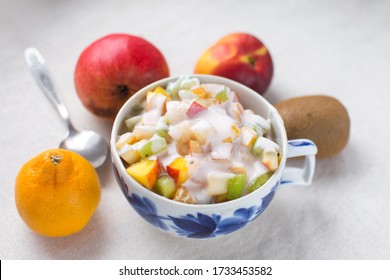 fruit salad serving in a Cup with fresh milk yogurt and a metal spoon isolate on a white background kiwi nectarine pear Mandarin