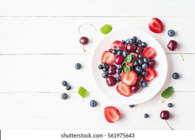 Fruit salad with strawberry, blueberry, sweet cherry on wooden white background. Flat lay, top view