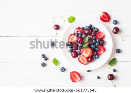 Fruit salad with strawberry, blueberry, sweet cherry on wooden white background. Flat lay, top view