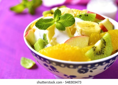 Fruit salad with yogurt and honey in a vintage bowl on a pink wooden table.