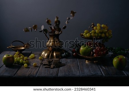 Fruit still life with grapes, apples, chocolate, eucalyptus and antique copper utensils on dark wooden table background