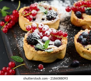 Fruit Tart With Red Currants Sprinkled With Powdered Sugar On A Black Table