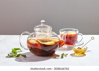 Fruit tea with apples and thyme and honey in glass teapot and cup on white background with hard shadows. - Shutterstock ID 2038166762