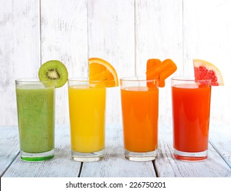 Fruit And Vegetable Juice In Glasses And Pieces Of Fresh Fruits On Wooden Table On Wooden Wall Background