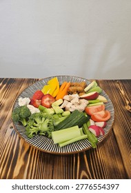 Fruit And Vegetable Selection Laid Out On Striped Plate On Wooden Table With White Wall Background  