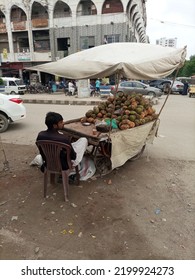 A Fruit Vendor Is Sitting Next To Wheel Cart Selling Coconut - Karachi Pakistan - Aug 2022