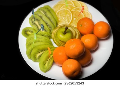 Fruit white plate with tangerines, kiwi, sliced apple and lemon slices on background isolated black. - Powered by Shutterstock