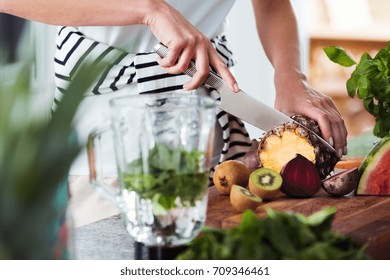 Fruitarian cutting pineapple on wooden board to prepare fresh smoothie with mint - Powered by Shutterstock