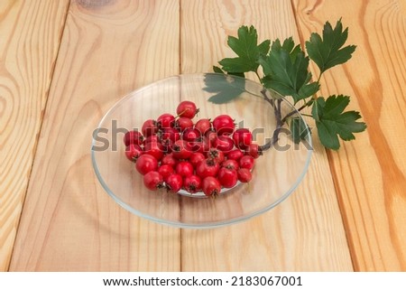 Fruits of the hawthorn on glass saucer and twig with leaves on the wooden rustic table  

