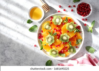 Fruits salad: kiwi, orange, pomegranate and mint served with honey. Healthy eating. Top view with copy space.