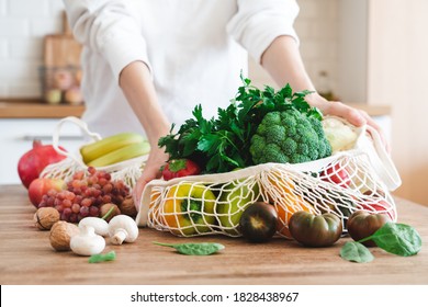 Fruits And Vegetables In Cotton Reusable Net Mesh Bag On Wooden Table In Modern Bright Kitchen. Organic Vegan Food Set. Sustainable Lifestyle Concept