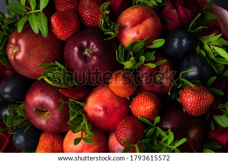 fruity bouquet of red apples with plums, red pepper, strawberry and pistachio branches. On a wooden table and gray background.