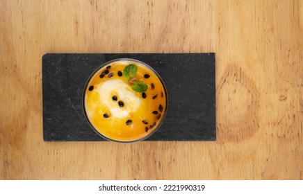 Fruity Desserts. Closeup View Of A Glass With Passion Fruit Mousse, In A Black Dish On The Wooden Table. 