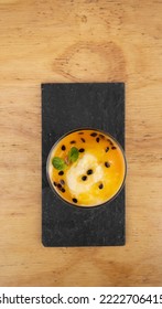 Fruity Desserts. Closeup View Of A Glass With Passion Fruit Mousse, In A Black Dish On The Wooden Table.