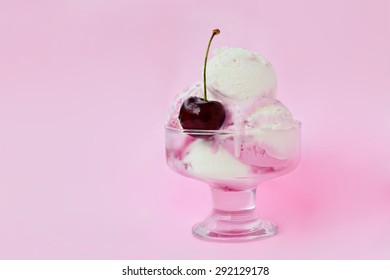 Fruity ice-cream with cherry in glass bowl on pink background.