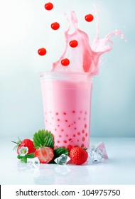 Fruity Pink Strawberry Boba Tea Splashing From A Glass With Falling Red Tapioca Pearls, Ice And Ripe Delicious Strawberries