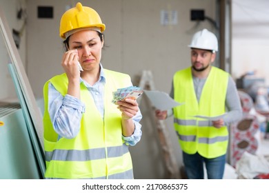 Frustrated adult female builder in yellow uniform standing at construction site indoors, holding banknotes and crying because of small salary - Shutterstock ID 2170865375