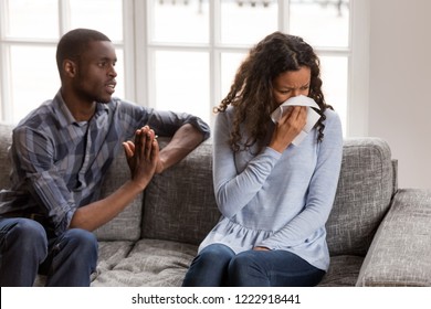 Frustrated African American man apologizing to woman after quarrel, crying wife with handkerchief in hands no desire to talk with husband feeling guilty, asking forgive, begging pardon, regret