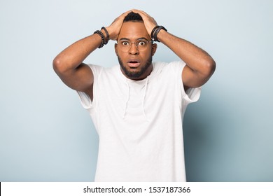 Frustrated african American man in glasses isolated on blue studio background round eyes feel scared afraid, confused biracial male in spectacles stunned shocked by unexpected news or information