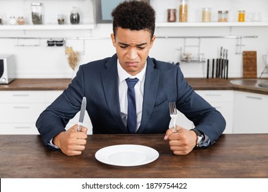 frustrated african american man holding cutlery and looking at empty plate - Powered by Shutterstock