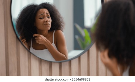 Frustrated African American woman suffer problem trouble curls looking at mirror at bathroom beauty routine prepare biracial girl female dry hair trying to brush combing curly tangled hairdo with comb - Powered by Shutterstock