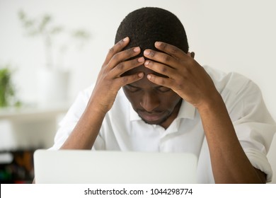 Frustrated african businessman feeling exhausted depressed holding head in hands sitting in front of laptop, hopeless stressed black man lost all money online, sad upset employee tired or overwork