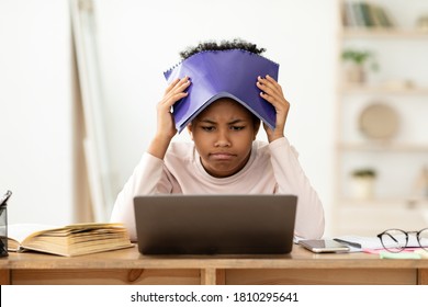 Frustrated African Kid At Laptop Getting Bad Grade During Online Class, Covering Head With Exercise-Book Sitting At Home. School Failure