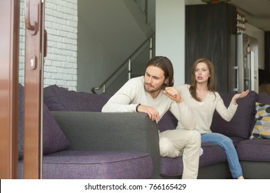 Frustrated angry man sitting on couch turned his back ignoring wife blaming shouting at him, young married couple having quarrel at home, unhappy husband and wife arguing, problems in relationships