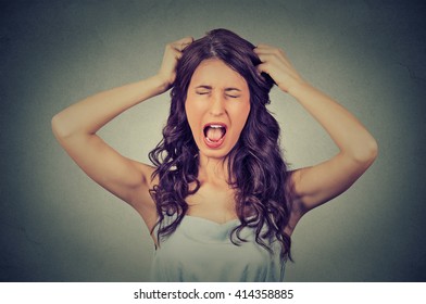 Frustrated And Angry Woman Is Screaming Out Loud And Pulling Her Hair Isolated On Gray Wall Background 