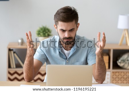 Frustrated annoying man sitting at the desk in office using computer, looking at broken crashed laptop feels anger and indignance. Worried male has verification password problems or data loss concept