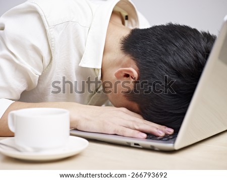 frustrated asian young man buries his head in the keyboard of a laptop computer.
