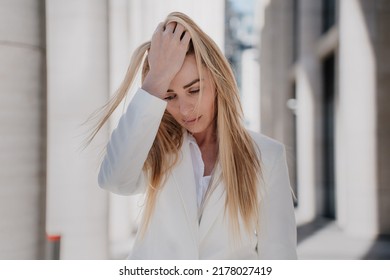 Frustrated blonde caucasian young woman walking eyes looking down with upset facial expression touching head, depressed, having financial problems. Beautiful swedish woman having headache outdoors.