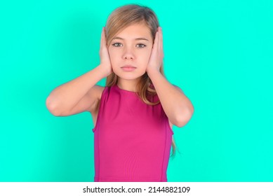 Frustrated Blonde Little Kid Girl Wearing Pink Sport Clothes Over Green Background Plugging Ears With Hands Does Not Wanting To Listen Hard Rock, Noise Or Loud Music.