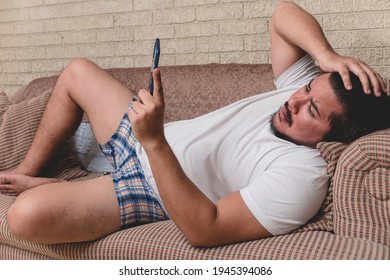 A Frustrated And Bothered Man Of Mixed Race Lying On The Couch Triggered By What He Sees On The Phone.