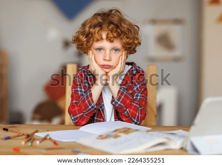 Frustrated boy thinking over difficult task and touching head while doing homework at table