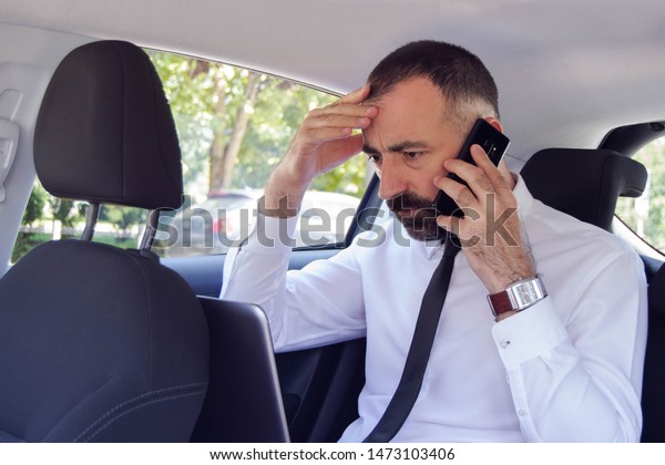 Frustrated business man / employee  talking on\
mobile phone while sitting in the back seat of car. He has a\
problem and doesn\'t know how to solve\
it.