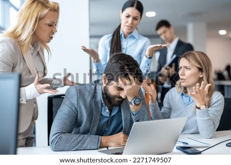Frustrated businessman covering face with hand, having serious problems while his co-workers making him feels guilty for not doing his job properly at office. Business conflict and overwork concept.