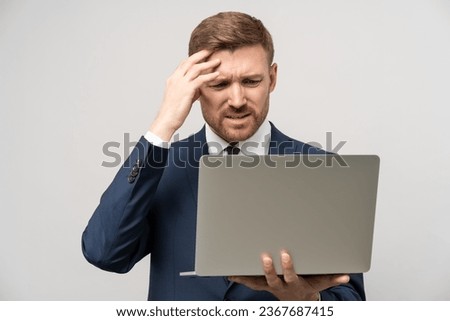 Frustrated businessman in emotional stress watching downfall stock market on laptop, lost money on falling stock prices. Furious trader man in costume think about problem isolated on studio gray wall.