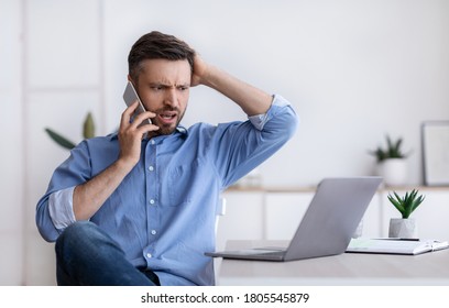 Frustrated Businessman Having Problems With Computer In Office, Talking On Cellphone With Customer Support, Looking At Laptop Screen With Shock