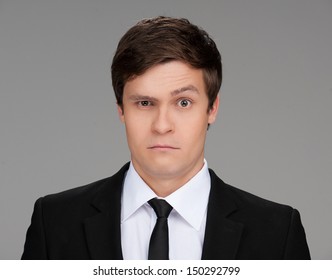 Frustrated businessman. Portrait of frustrated young businessman looking at camera while isolated on grey