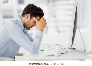 Frustrated businessman sitting on desk with hand on head in office - Shutterstock ID 571110763