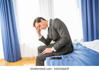 Frustrated Businessman Sitting On The Hotel Bed Holding His Hand On Head