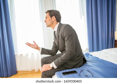 Frustrated Businessman Sitting On The Hotel Bed Holding His Hand On Head