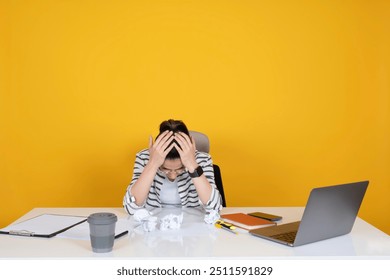 Frustrated businesswoman, portrait of young caucasian frustrated businesswoman sit office desk holding head in hands over yellow studio background copy space. Crumpled papers, work problems concept. - Powered by Shutterstock