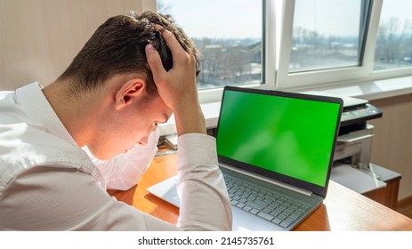 A frustrated Caucasian holds his head while receiving bad news while sitting at a table in front of a computer with a green screen. High quality photo - Powered by Shutterstock