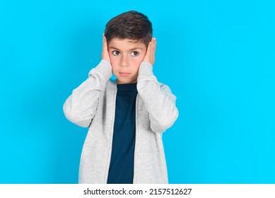 Frustrated Caucasian Kid Boy Wearing Grey Hoodie Over Blue Background Plugging Ears With Hands Does Not Wanting To Listen Hard Rock, Noise Or Loud Music.