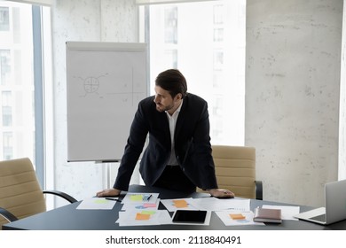 Frustrated concerned business man standing at table with sales reports, paper sticky notes, looking away, thinking over company future, negative statistics result, financial loss - Shutterstock ID 2118840491